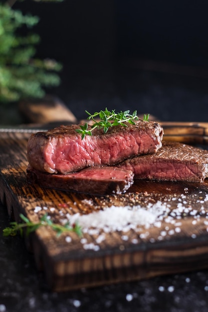 Mediumrare sliced beef steak with salt and herbs on a wooden board on a dark background