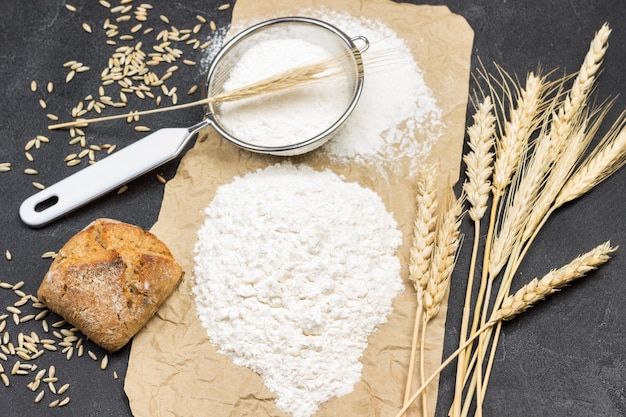 Meel, aartjes tarwe, brood en zeef op bruin papier. Bovenaanzicht