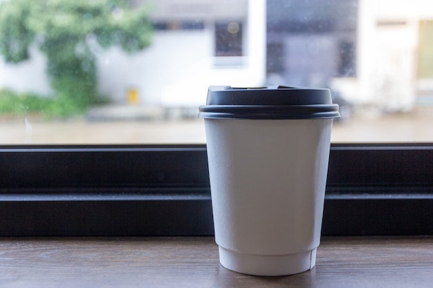 Meeneemkoffiekop op de houten lijst dichtbij het venster