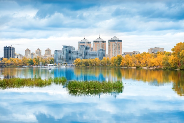 Meer met blauw water, herfstgeel bos en hoge gebouwen op andere oever