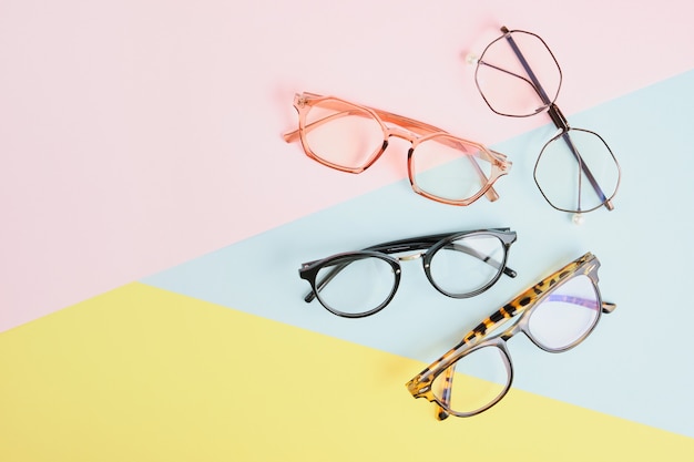 Meerdere brillen op een veelkleurige achtergrond van pastelkleuren, geometrische achtergrond, roze gele en lichtblauwe kleuren, trendy brilmonturen kopiëren ruimte