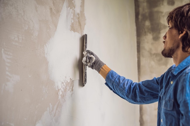 Meester brengt witte stopverf op een muur aan en smeert overdag met een plamuurmes in een kamer van het renoveren van een huis