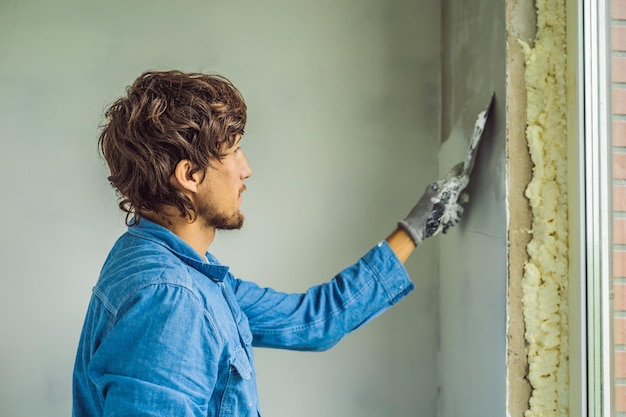 Foto meester brengt witte stopverf op een muur aan en smeert overdag met een plamuurmes in een kamer van het renoveren van een huis