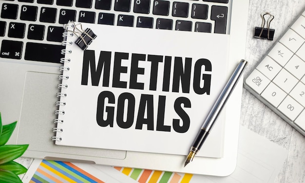 MEETING GOALS text on white paper and laptop on wooden background