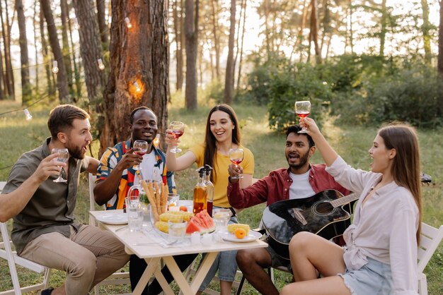 Meeting of multiracial group of friends playing guitar singing eating dinner and drinking wine