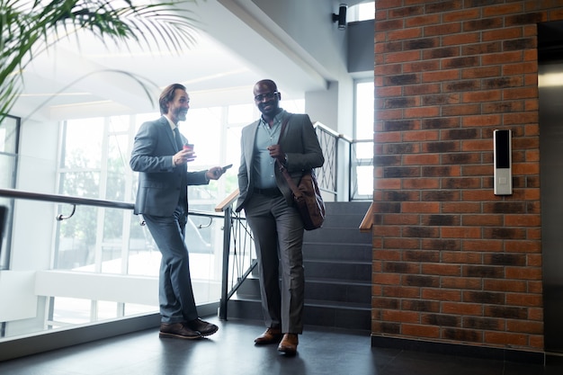 Meeting near elevator. Two businessmen wearing suits smiling while meeting near the elevator