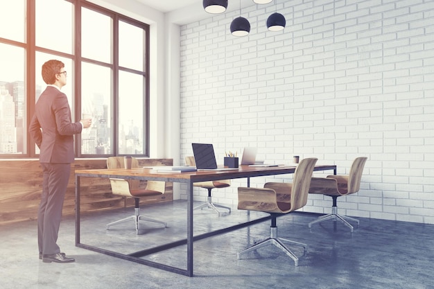 Meeting room interior with white brick walls, a concrete floor, large windows and a long wooden table with wooden chairs near it. 3d rendering mock up toned image