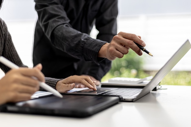 Meeting room of a startup company where businessmen are pointing at their laptop screens to see company financial summaries, they are meeting on monthly finance topics. Concept of financial management