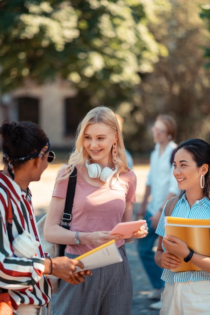 Meeting in the yard. Two smiling girls speaking with their joyful groupmate going home after university.