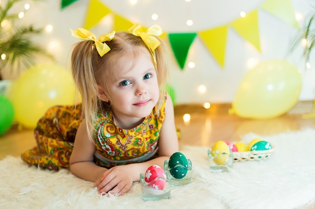 Meisje 3 jaar oud liggend op de vloer met heldere gele kleren met paaseieren