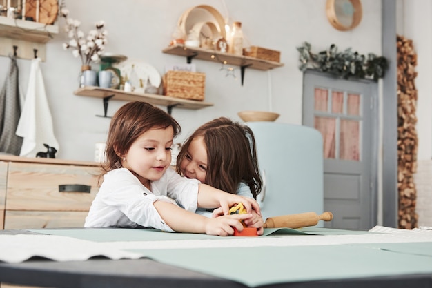 Meisje aan de rechterkant lacht en wil plezier hebben. Twee kinderen spelen met geel en oranje speelgoed in de witte keuken.