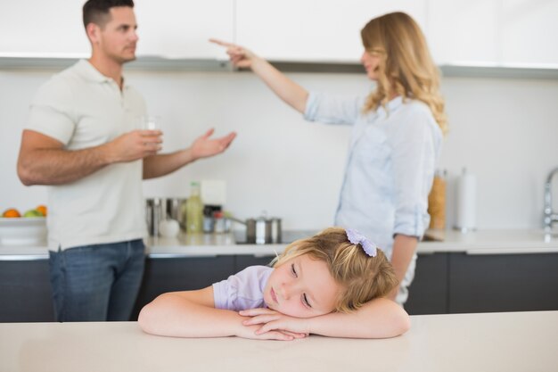 Meisje aan tafel met ouders ruzie op achtergrond