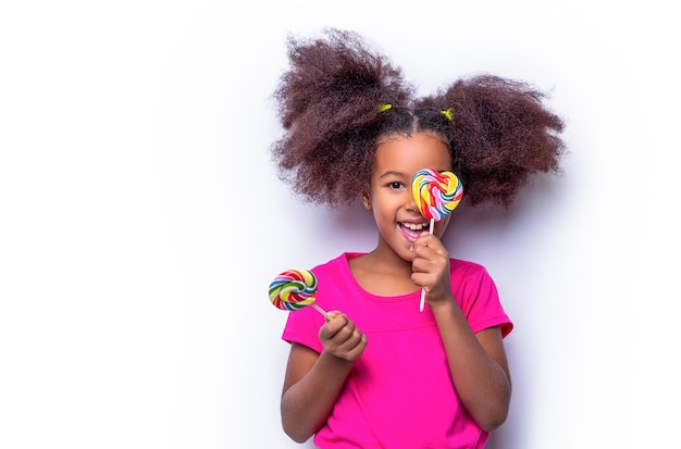 Meisje afro lolly's Glimlach klein Afrikaans Amerikaans meisje dat lolly eet met roze zoete kleurrijke lolly snoep snoepjes Schattig multiraciaal klein meisje lachende lolly in de hand op achtergrond