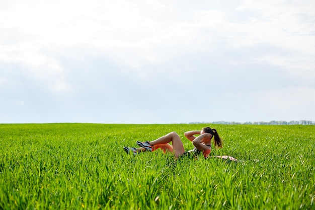 Meisje atleet schudt de pers ligt op een tapijt in de natuur. Jonge vrouw gaat voor sport, gezonde levensstijl, atletisch lichaam.