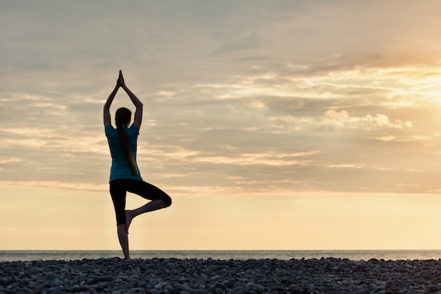 Meisje bij zonsondergang het beoefenen van yoga aan de kust, achteraanzicht