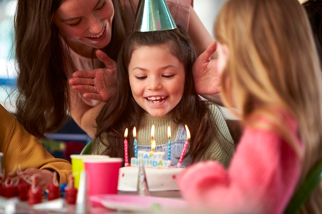 Meisje blaast kaarsjes uit op verjaardagstaart op feestje met ouders en vrienden thuis