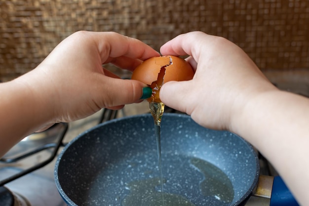 Meisje breekt een ei over een pan met plantaardige olie.