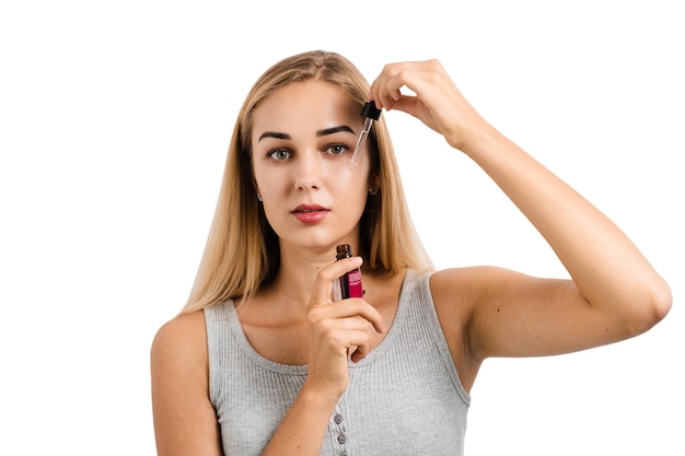 Meisje brengt gezichtsserum aan op haar gezicht met pipet op witte achtergrond Jonge vrouw maakt verjongende cosmetische ingreep voor huid en gezicht