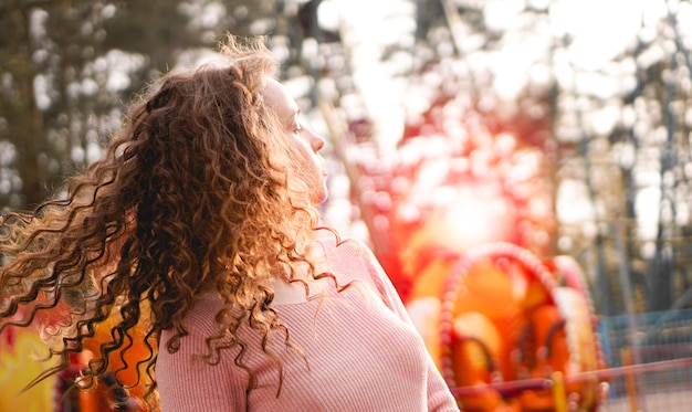 Meisje chillen in pretpark in weekendochtend. lachend goedgehumeurd vrouwelijk model met krullend haar dat zich dichtbij carrousel bevindt.