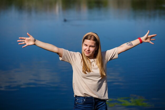 Foto meisje dansen in de buurt van het meer, zonnig weer. een jonge vrouw verheugt zich in het leven, danst en zingt. ze heeft een goed humeur en een glimlach op haar gezicht.