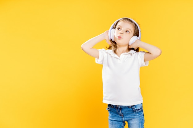 Meisje dat aan muziek in draadloze hoofdtelefoons op geel luistert. Dansend meisje. Gelukkig klein meisje dat op muziek danst. Leuk kind dat van gelukkige dansmuziek geniet.