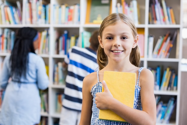 Meisje dat een boek in bibliotheek houdt