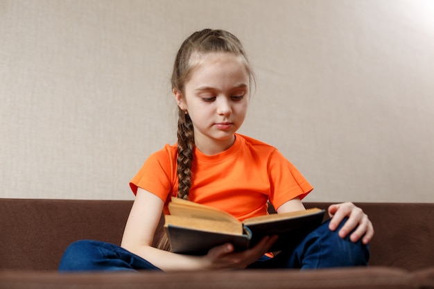 Meisje dat een boek op de bank leest. kaukasisch meisje die alleen tijd doorbrengen die op de laag met een oud boek ontspannen.