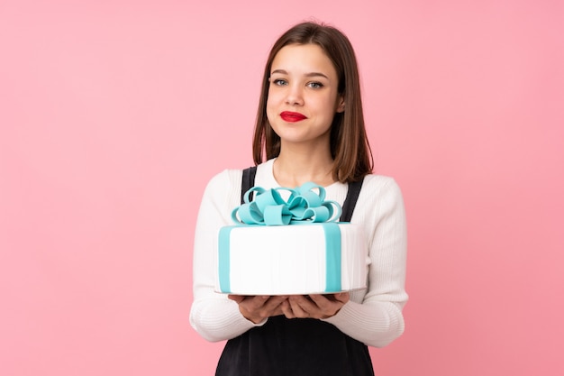 Meisje dat een grote cake op roze muur houdt die veel glimlacht