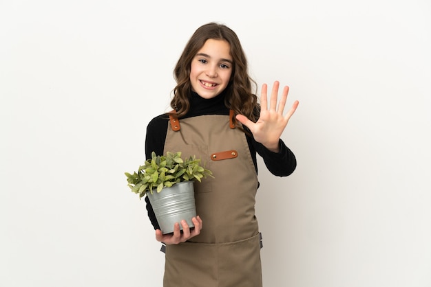 Meisje dat een plant houdt die op witte muur wordt geïsoleerd die vijf met vingers telt
