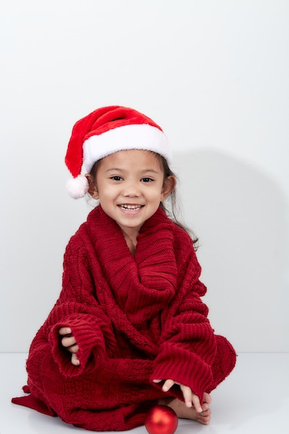 Meisje dat een rode Kerstmisbal in sweater en santahoed houdt