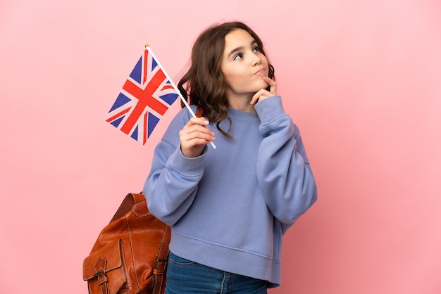 Meisje dat een vlag van het Verenigd Koninkrijk houdt die op roze achtergrond wordt geïsoleerd die twijfels heeft terwijl het opzoeken