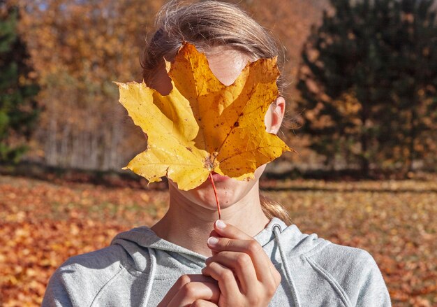 Foto meisje dat gezicht bedekt met esdoornblad