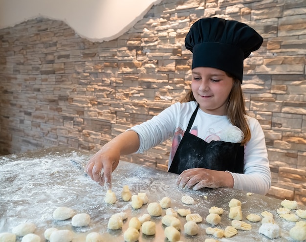 Meisje dat gnocchi kneedt verkleed als chef-kok