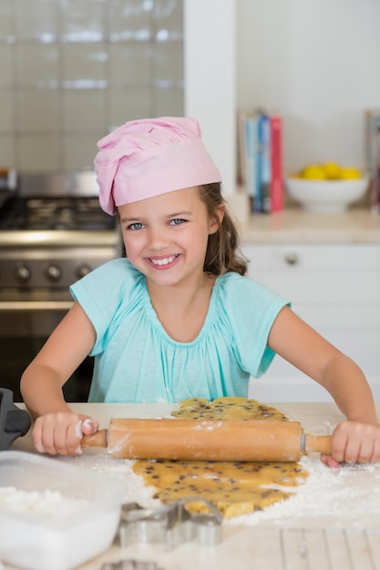 Meisje dat het deeg met een deegrol in de keuken afdekt