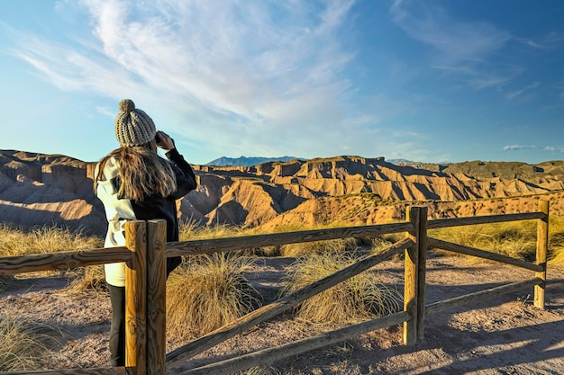 Meisje dat het woestijnlandschap observeert, leunend op een houten hek met een verrekijker
