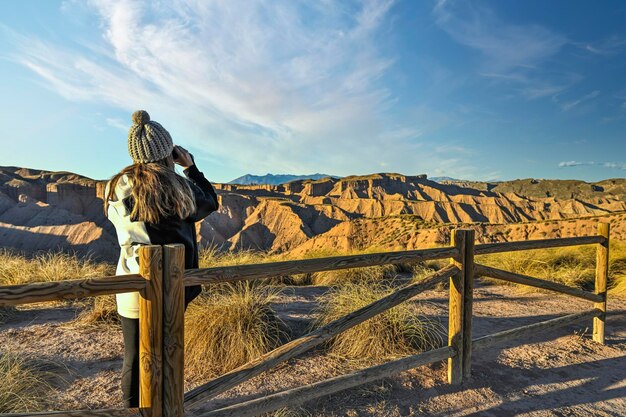 Meisje dat het woestijnlandschap observeert, leunend op een houten hek met een verrekijker