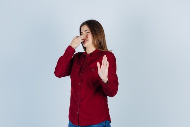 meisje dat iets vreselijks ruikt, neus knijpt, stopbord toont in casual shirt en er walgelijk uitziet.