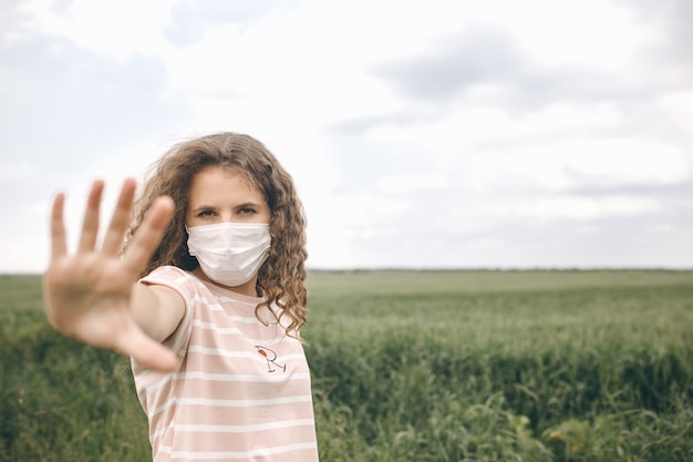 Meisje dat in een groen veld in een beschermend masker staat, toont stophand om het coronavirus te stoppen