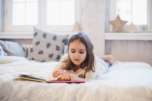 Meisje dat met kerstmis een boek op het bed leest