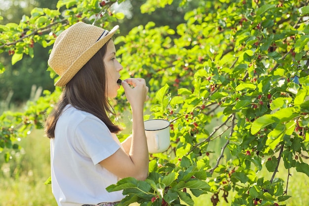 Meisje dat met plezier heerlijke zoete rijpe bessen van de moerbeiboom eet. Zomerseizoen in de tuin, natuurlijke biologische bessen, rijk aan vitamines, gezond voedsel