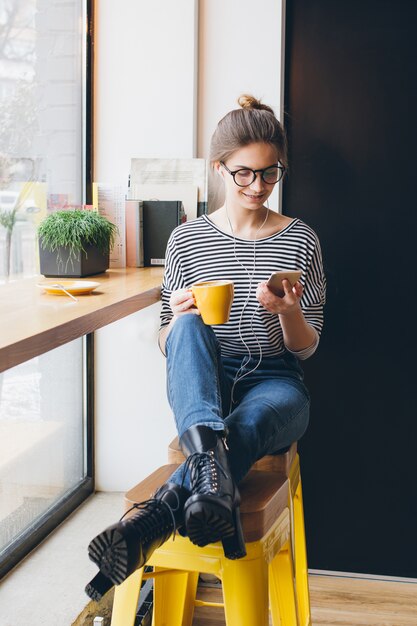 Meisje dat naar muziek op uw smartphone luistert en koffie drinkt