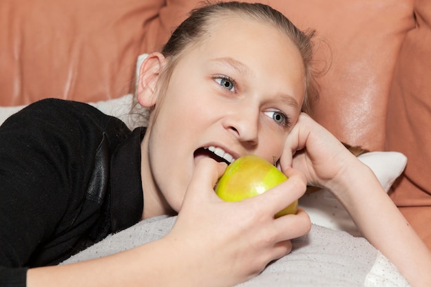 Meisje dat op de bank ligt die een appel eet