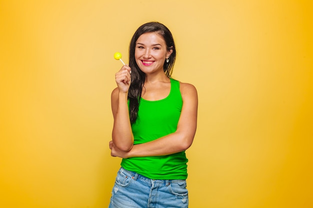 Meisje dat op gele achtergrond in groen t-shirt Lolly eet