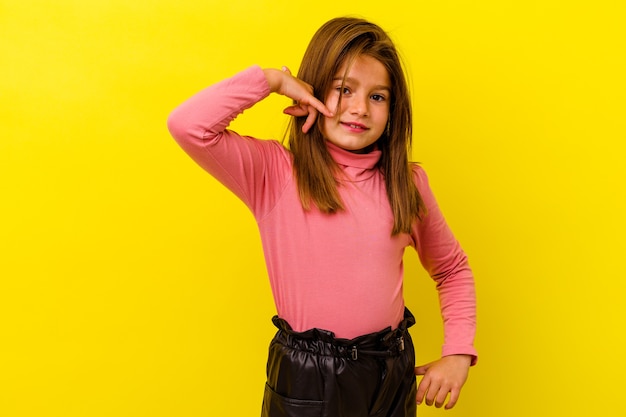 Meisje dat op gele muur wordt geïsoleerd die een gebaar van het mobiele telefoongesprek met vingers toont