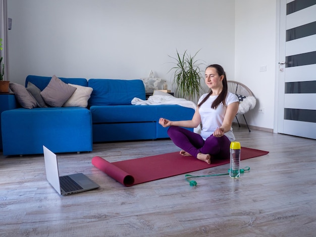 Meisje dat op laptop kijkt tijdens het beoefenen van yoga thuis