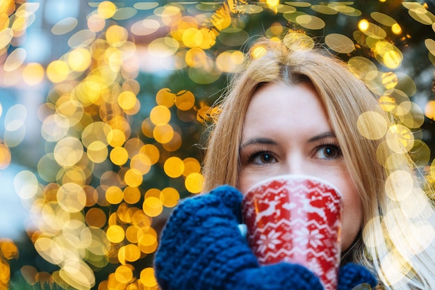 Foto meisje dat 's avonds in de winter op de traditionele kerstmarkt loopt, versierd met vakantieverlichting