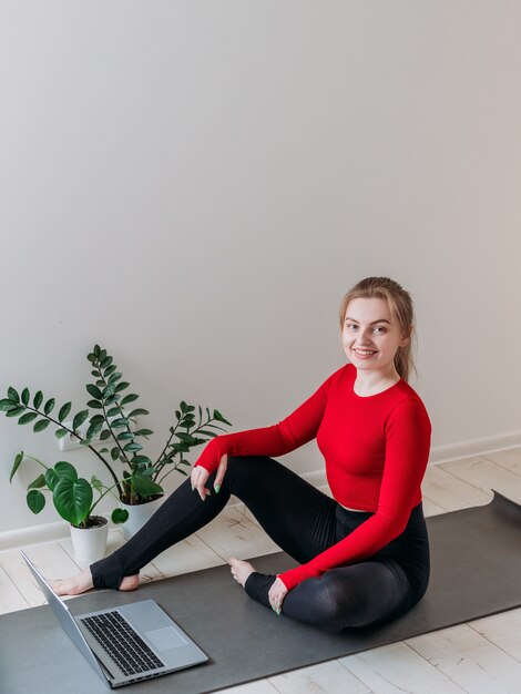 Meisje dat thuis yoga beoefent. Vrouw kijkt naar video op internet en herhaalt de taken. Binnen en buiten trainen. Sport en gezond actief levensstijlconcept.