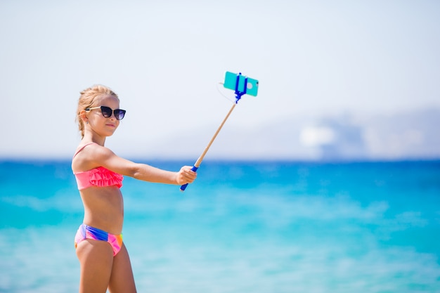 Meisje dat zelfportret neemt door haar smartphone op het strand. kind geniet van haar suumer vakantie en maakt foto's ter herinnering