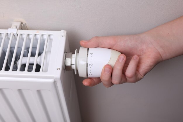 Meisje die de thermostaat van de verwarmingsradiator aanpassen dichtbij witte muur binnenshuis close-up