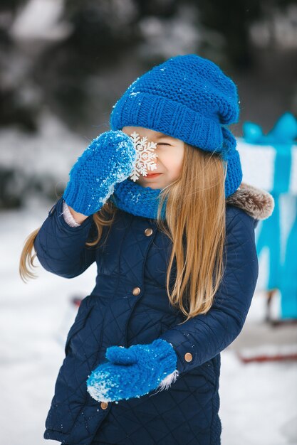 Meisje die een Kerstmisgift in haar handen houden en emothionally glimlachen. Kind draagt een blauwe gebreide muts, handschoenen, wanten, sjaal